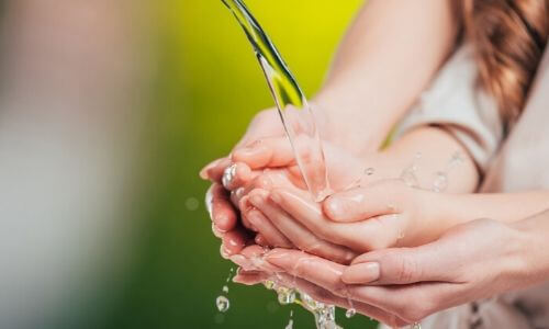 Hands under running water, emphasizing plumbing hygiene and maintenance, relevant to sink care and prevention of clogs.