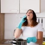 A woman in blue rubber gloves talks on a smartphone in a modern kitchen, showcasing Zing Plumbing's leak detection services.