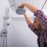Man adjusting showerhead in a bathroom, showcasing Zing Plumbing's expertise in shower systems and home improvement.