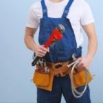Male plumber in blue overalls uses red wrench and tools in belt for plumbing tasks at Zing Plumbing service in Tucson, AZ.