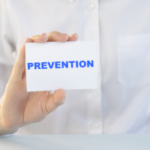 A person in a white shirt holding a blue "PREVENTION" card, discussing Zing Plumbing's garbage disposal maintenance tips.