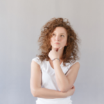 A woman with curly hair in a white T-shirt contemplating garbage disposal maintenance for the holiday season.