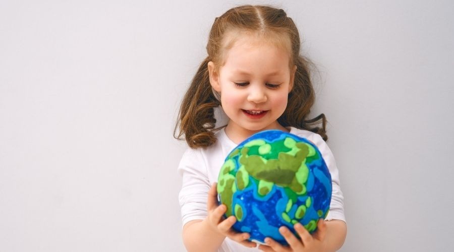 Young girl holding a globe with oceans and landmasses, against a light wall. Zing Plumbing press release image.