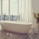 Freestanding bathtub near large windows and potted plant, showcasing water conservation tips with Zing Plumbing.