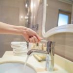 A hand turning on a faucet over a bathroom sink, representing water conservation tips from Zing Plumbing in Tucson, AZ.