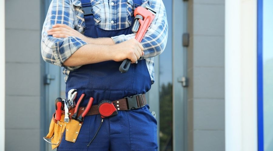 Tradesperson in blue uniform with tools, standing confidently near a modern building for Zing Plumbing services.