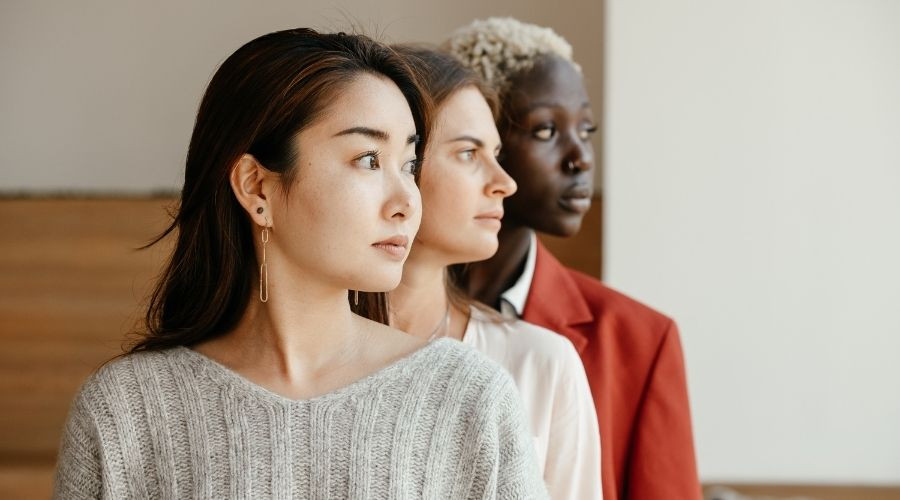 Three diverse women in casual and formal attire, united in diversity with thoughtful expressions.