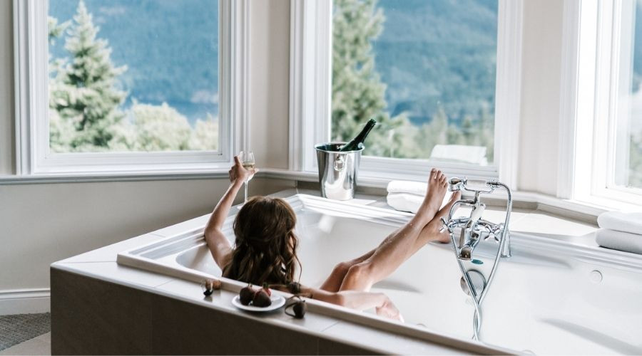 Person relaxing in a luxurious bathtub with champagne and strawberries, showcasing Zing Plumbing's upscale bathroom design.