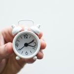 White alarm clock held by a hand, symbolizing urgency in plumbing repairs by Zing Plumbing in Tucson, AZ.