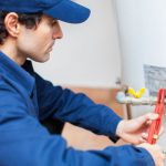 Plumber adjusting a water heater, wearing a blue uniform, demonstrating skilled labor in plumbing services.