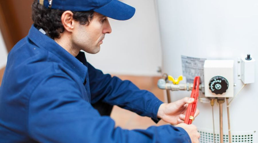 Professional plumber in blue uniform repairing water heater with tools at Zing Plumbing service.