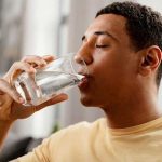 Young man enjoying a glass of water indoors, highlighting Zing Plumbing's focus on water quality and filtration systems.