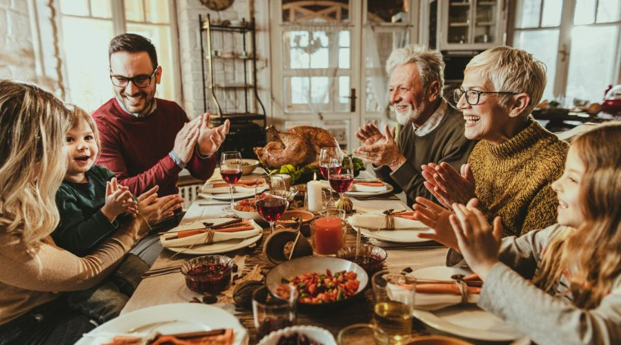 Diverse group gathered around a dining table with roasted turkey, highlighting holiday celebrations by Zing Plumbing.