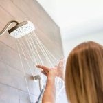 Woman enjoying a modern shower with flowing water and damp hair, reflecting a fresh bathroom atmosphere by Zing Plumbing.