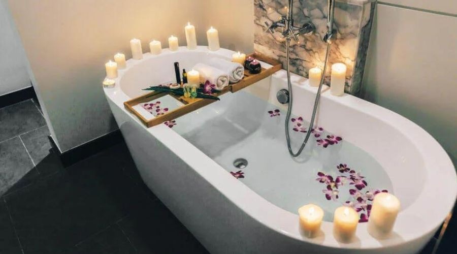 Oval bathtub with rose petals and candles, plus a wooden caddy for toiletries—Zing Plumbing service.