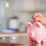 Piggy bank on kitchen counter with coins, symbolizing saving tips by Zing Plumbing for reducing summer water bills.
