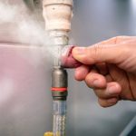 Hand adjusting a valve in a plumbing system, with steam escaping, showcasing Zing Plumbing's gas line safety services.