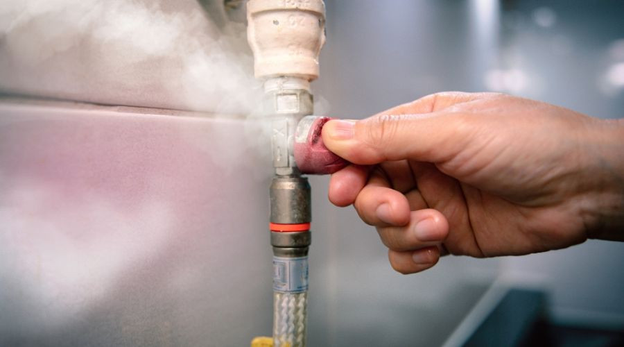 Hand gripping a valve on a steam-emitting pipe fitting, representing urgent plumbing maintenance by Zing Plumbing.