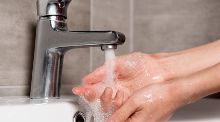 A person rinsing soap suds off their hands under running water from a bathroom sink faucet.