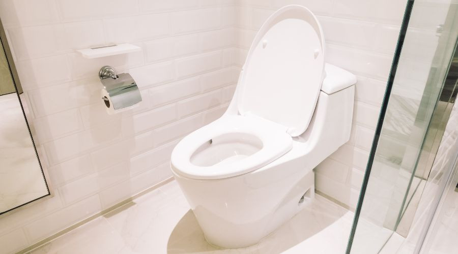 Modern toilet in a minimalist bathroom, featuring white tiles and a sleek design; plumbing tips resource by Zing Plumbing.